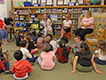  Students sitting in library listening to a retiree read a book.